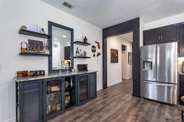 bar with visible vents, stainless steel refrigerator with ice dispenser, a bar, a textured ceiling, and dark wood finished floors