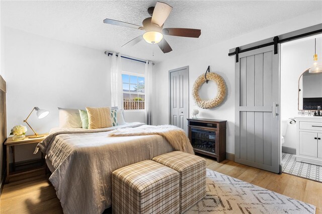 1202 Anderson St, Deltona, FL 32725 - bedroom featuring light wood-style flooring, a textured ceiling, a ceiling fan, ensuite bathroom, and a barn door