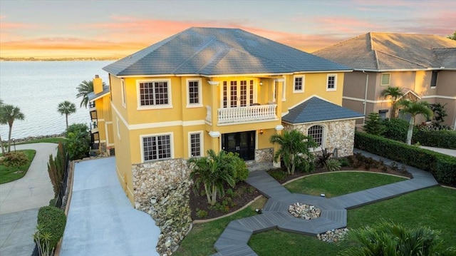 view of front of home featuring stucco siding, stone siding, a water view, and a balcony