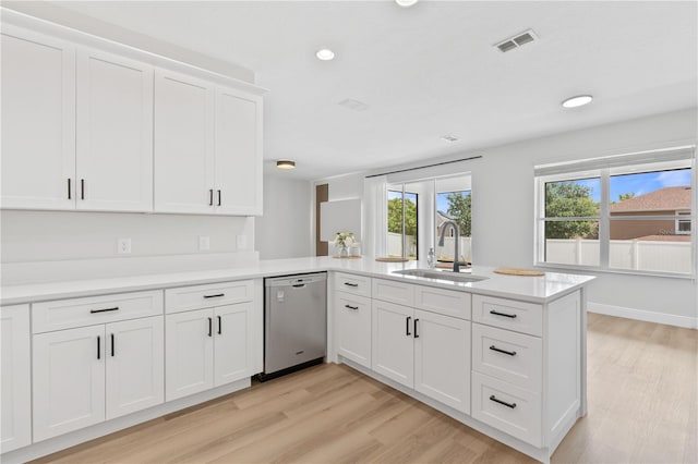 kitchen with stainless steel dishwasher, a sink, light wood-style floors, and a peninsula
