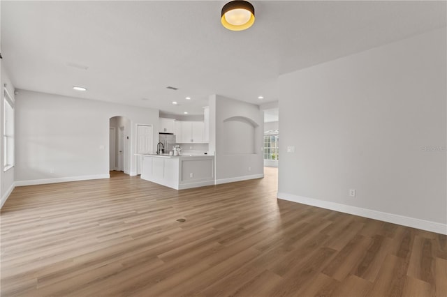 unfurnished living room with recessed lighting, arched walkways, baseboards, and light wood-type flooring