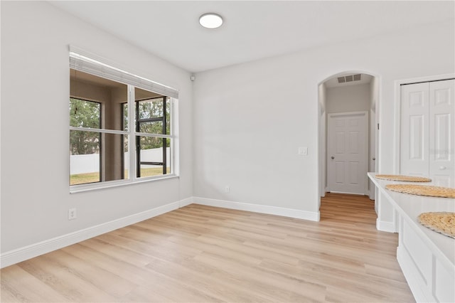 spare room with arched walkways, light wood-style floors, visible vents, and baseboards
