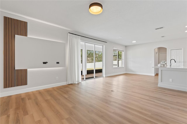 unfurnished living room with visible vents, a sink, baseboards, light wood-type flooring, and arched walkways