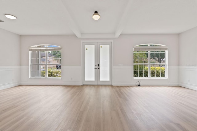 entrance foyer with french doors, wainscoting, a decorative wall, and wood finished floors