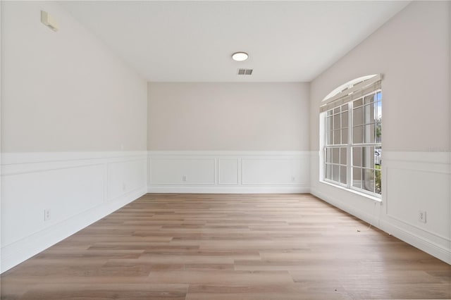unfurnished room featuring visible vents, light wood-style flooring, and wainscoting
