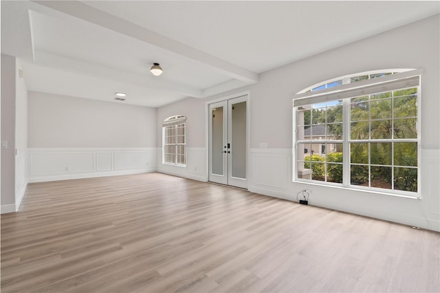 spare room with french doors, light wood-style flooring, beam ceiling, and wainscoting