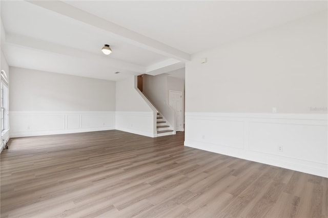 unfurnished room with stairway, beam ceiling, wainscoting, and wood finished floors
