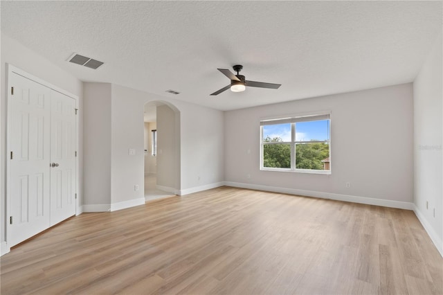 unfurnished bedroom featuring visible vents, arched walkways, light wood finished floors, and baseboards