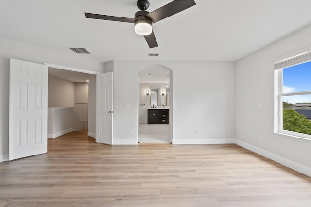 unfurnished bedroom with visible vents, arched walkways, light wood finished floors, and ensuite bath