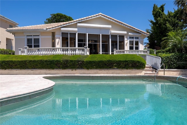 rear view of house with a tile roof, an outdoor pool, and stucco siding