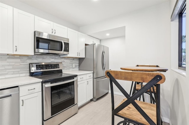 kitchen featuring light countertops, appliances with stainless steel finishes, white cabinetry, backsplash, and light wood-style flooring