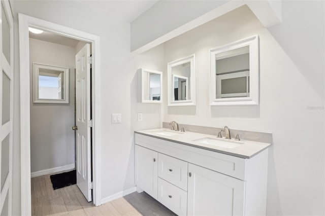 full bath featuring a sink, baseboards, double vanity, and wood finished floors