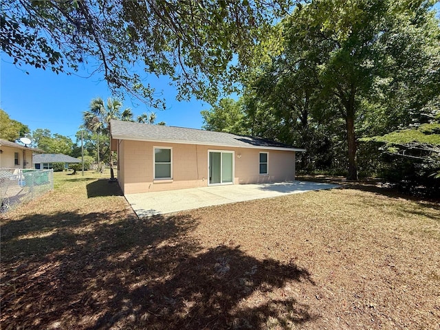 rear view of house with a patio area, concrete block siding, fence, and a yard
