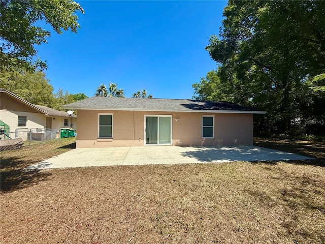 rear view of house with a patio area, concrete block siding, fence, and a shingled roof