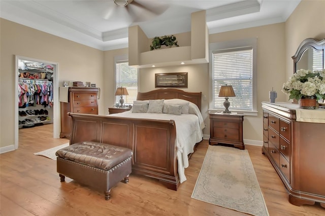 bedroom featuring a walk in closet, light wood finished floors, baseboards, ornamental molding, and a closet