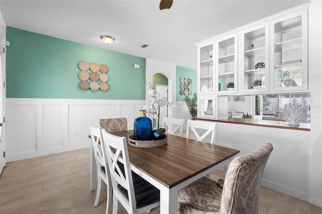 dining room featuring wainscoting, visible vents, arched walkways, and a decorative wall