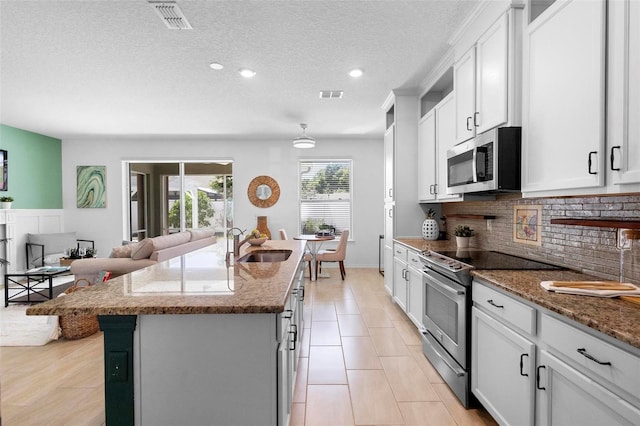 kitchen featuring a sink, visible vents, decorative backsplash, an island with sink, and appliances with stainless steel finishes