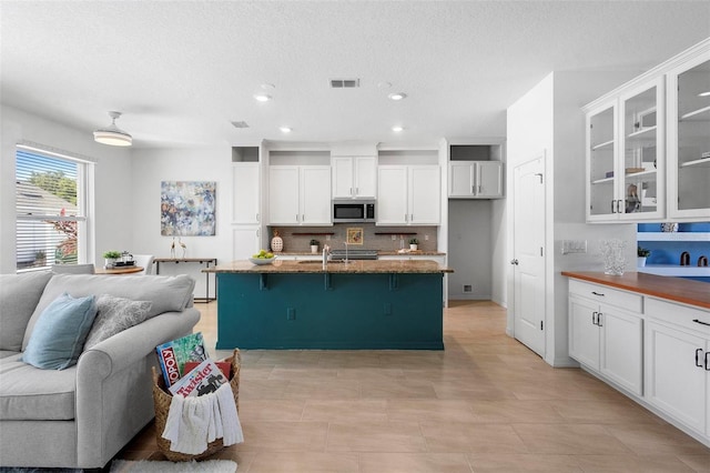 kitchen with stainless steel microwave, open floor plan, visible vents, backsplash, and white cabinetry