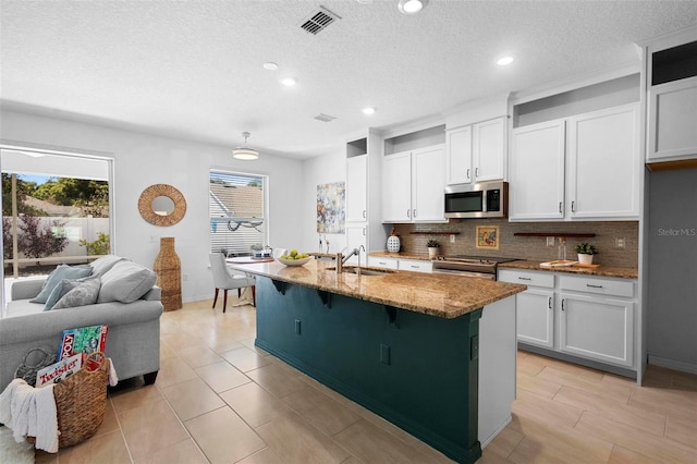 kitchen featuring light stone counters, visible vents, a sink, decorative backsplash, and appliances with stainless steel finishes