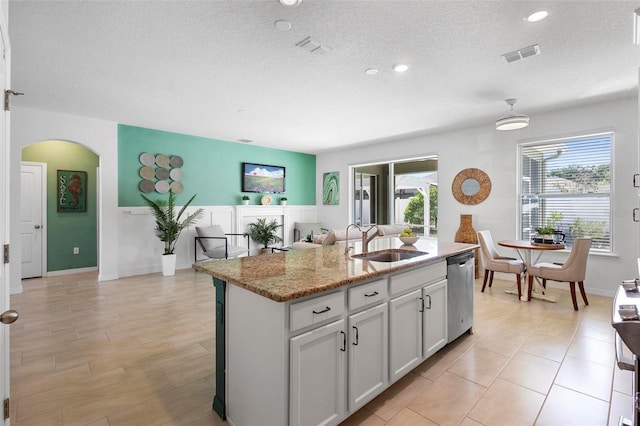 kitchen with arched walkways, a textured ceiling, stainless steel dishwasher, and a sink