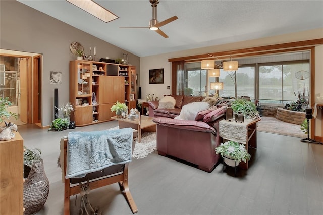 living area featuring ceiling fan, a wealth of natural light, vaulted ceiling with skylight, and wood finished floors