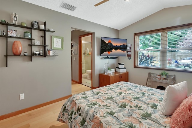 bedroom featuring baseboards, visible vents, light wood-style floors, lofted ceiling, and ensuite bath