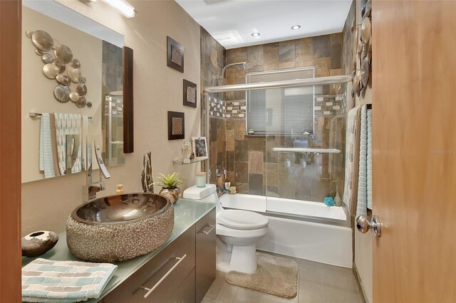 bathroom with tile patterned floors, vanity, shower / bath combination with glass door, and toilet
