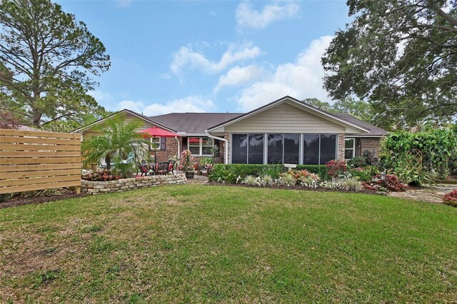 back of property with brick siding, a yard, a sunroom, and fence