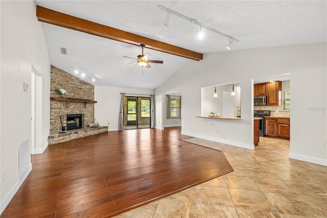 unfurnished living room with track lighting, plenty of natural light, lofted ceiling with beams, and ceiling fan