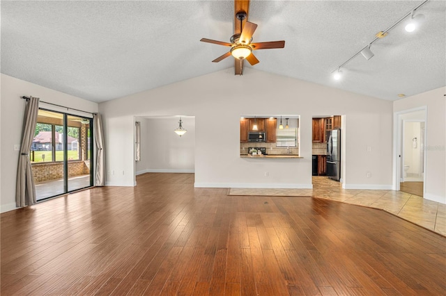 unfurnished living room with lofted ceiling, baseboards, light wood-type flooring, a textured ceiling, and a ceiling fan