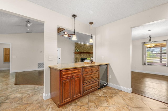 kitchen featuring brown cabinetry, visible vents, a fireplace, ceiling fan, and a textured ceiling