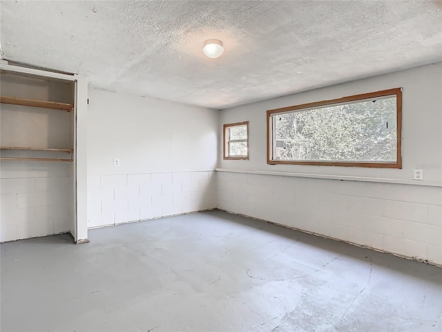 unfurnished bedroom featuring concrete floors, concrete block wall, a textured ceiling, and a closet