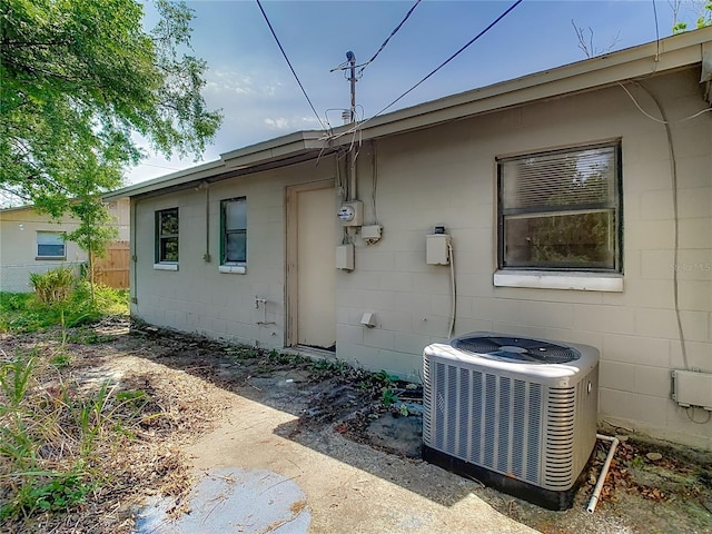 rear view of house with central AC, fence, and concrete block siding