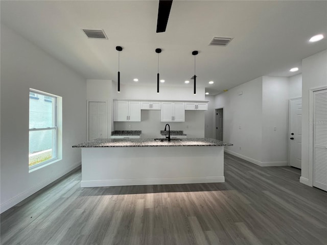 516 Model St, Daytona Beach, FL 32114 - kitchen with white cabinets, wood finished floors, a large island with sink, recessed lighting, and light stone counters