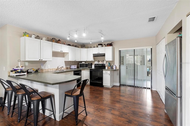 kitchen with a peninsula, a sink, visible vents, under cabinet range hood, and black appliances