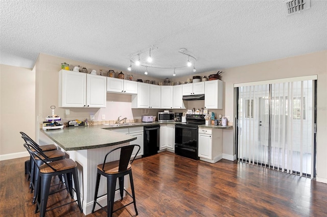 kitchen featuring a breakfast bar, visible vents, black appliances, a peninsula, and white cabinetry