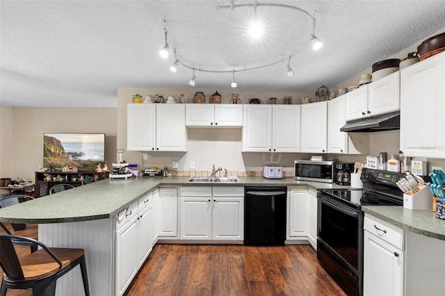 kitchen with a sink, black appliances, dark wood finished floors, a peninsula, and under cabinet range hood
