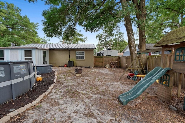 rear view of property with central AC, a playground, a fenced backyard, metal roof, and stucco siding