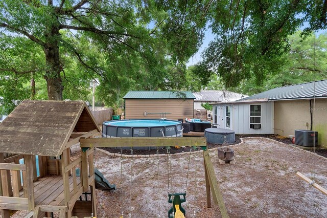 rear view of house featuring central AC unit, fence, an outdoor pool, and an outbuilding