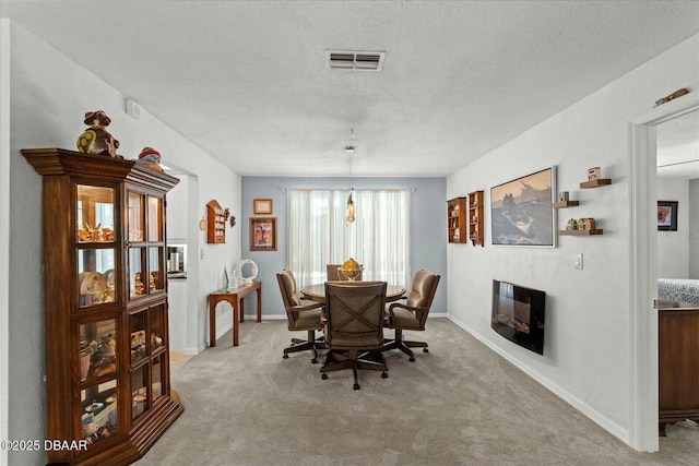 dining space featuring a textured ceiling, carpet floors, visible vents, and a glass covered fireplace