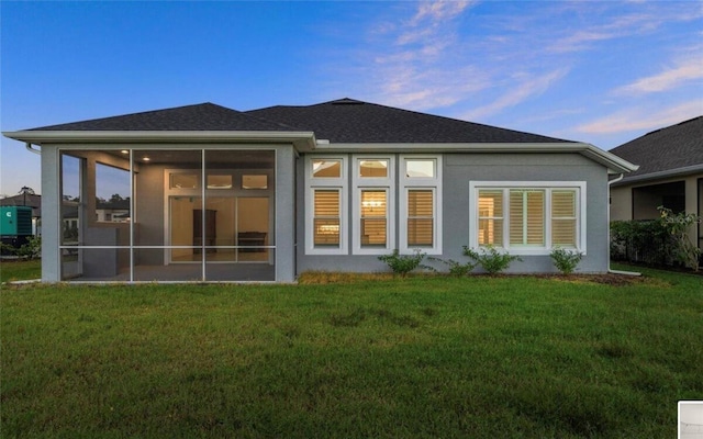 back of house at dusk featuring a yard, a sunroom, and stucco siding