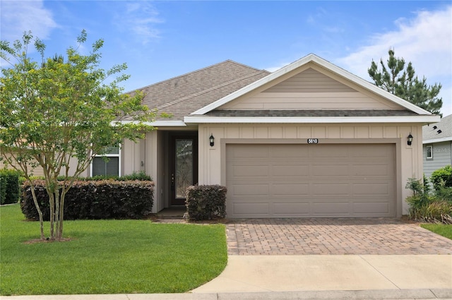 single story home with a shingled roof, decorative driveway, a front yard, and a garage