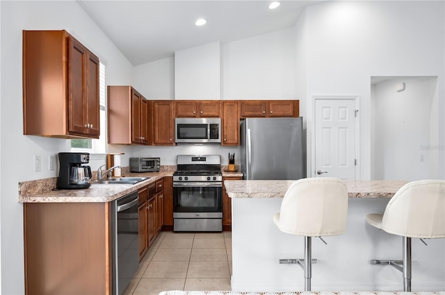 kitchen with a breakfast bar area, stainless steel appliances, a sink, high vaulted ceiling, and light countertops