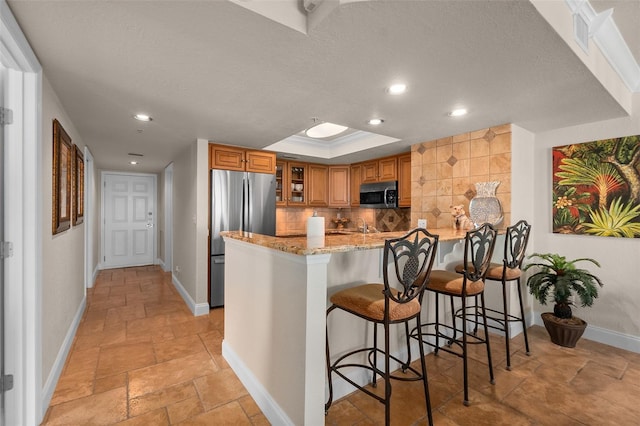 kitchen featuring light stone counters, appliances with stainless steel finishes, baseboards, a peninsula, and brown cabinetry