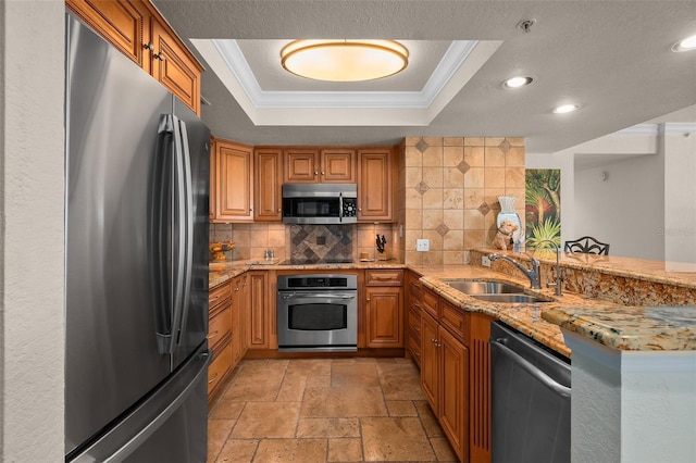 kitchen with a sink, stone tile flooring, stainless steel appliances, a tray ceiling, and recessed lighting