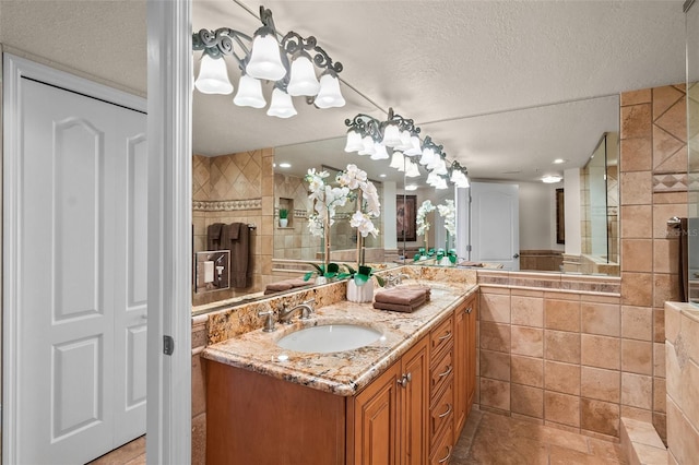 bathroom featuring double vanity, tile walls, a sink, a notable chandelier, and a textured ceiling