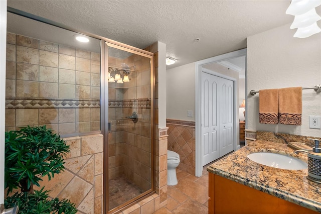 bathroom featuring tile walls, toilet, vanity, a stall shower, and a textured ceiling