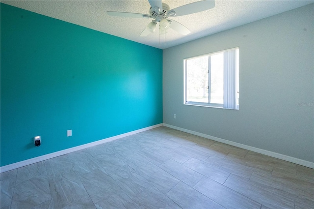 empty room with a textured ceiling, a ceiling fan, and baseboards