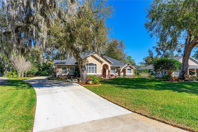 ranch-style home with stucco siding, stone siding, a front lawn, and concrete driveway