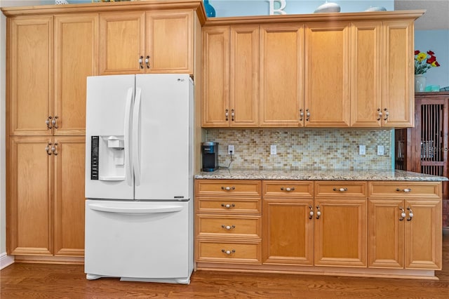 kitchen featuring backsplash, light stone counters, wood finished floors, and white refrigerator with ice dispenser